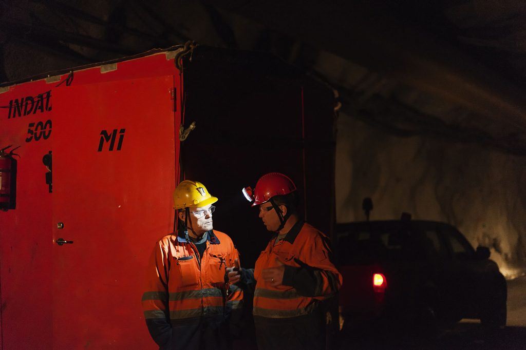 Two workers at night with headlamps talking in front of a battery storage unit.