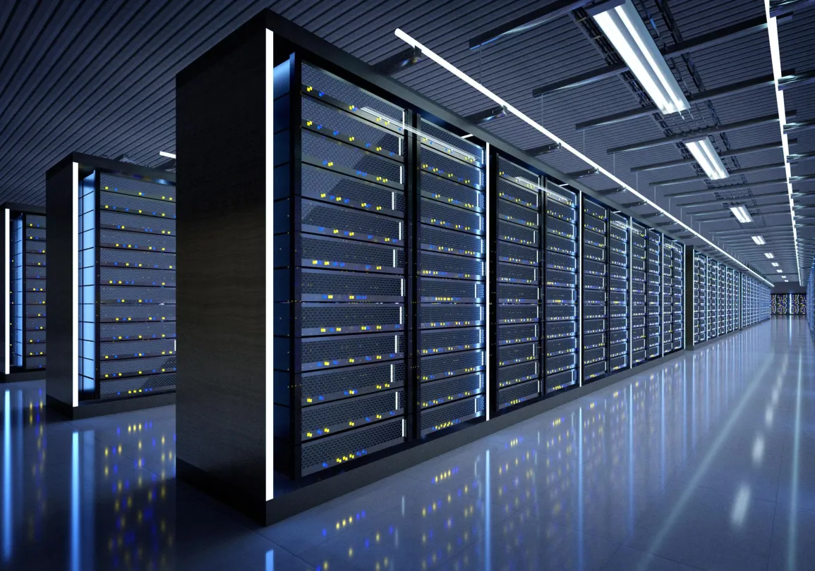 A modern data center with rows of server racks illuminated by blue and white lights. The floor is reflective, enhancing the glow from the server lights. The ceiling has evenly spaced fluorescent lights, and the room appears spacious and organized.