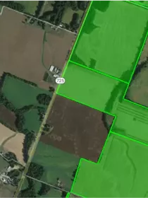 Aerial view of farmland with a road labeled 725 running vertically. Fields are divided by bright green lines, indicating property boundaries. The landscape includes various shades of green and brown, showing different types of vegetation and soil.