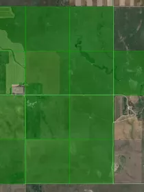 Aerial view of farmland divided into rectangular plots, highlighted in green. The plots contain various patterns of cultivation, surrounded by uncultivated land and a river running through the landscape.