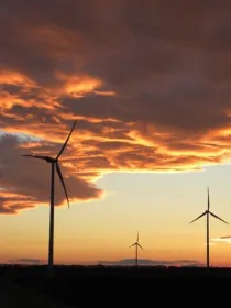 Wind turbines silhouetted against a dramatic sunset sky with orange and purple clouds.