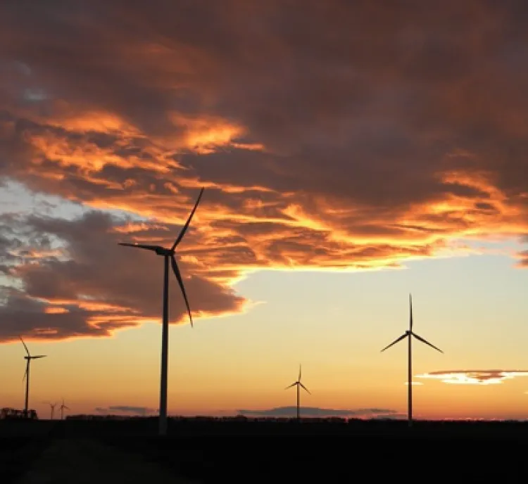 Silhouetted wind turbines under a dramatic sunset with orange and purple clouds.