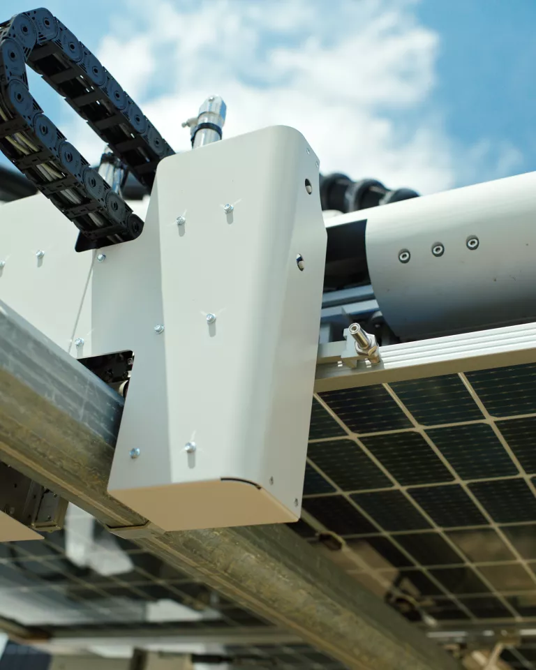 Close-up view of a solar panel installation showing metal supports, wiring, and mechanical components against a blue sky.