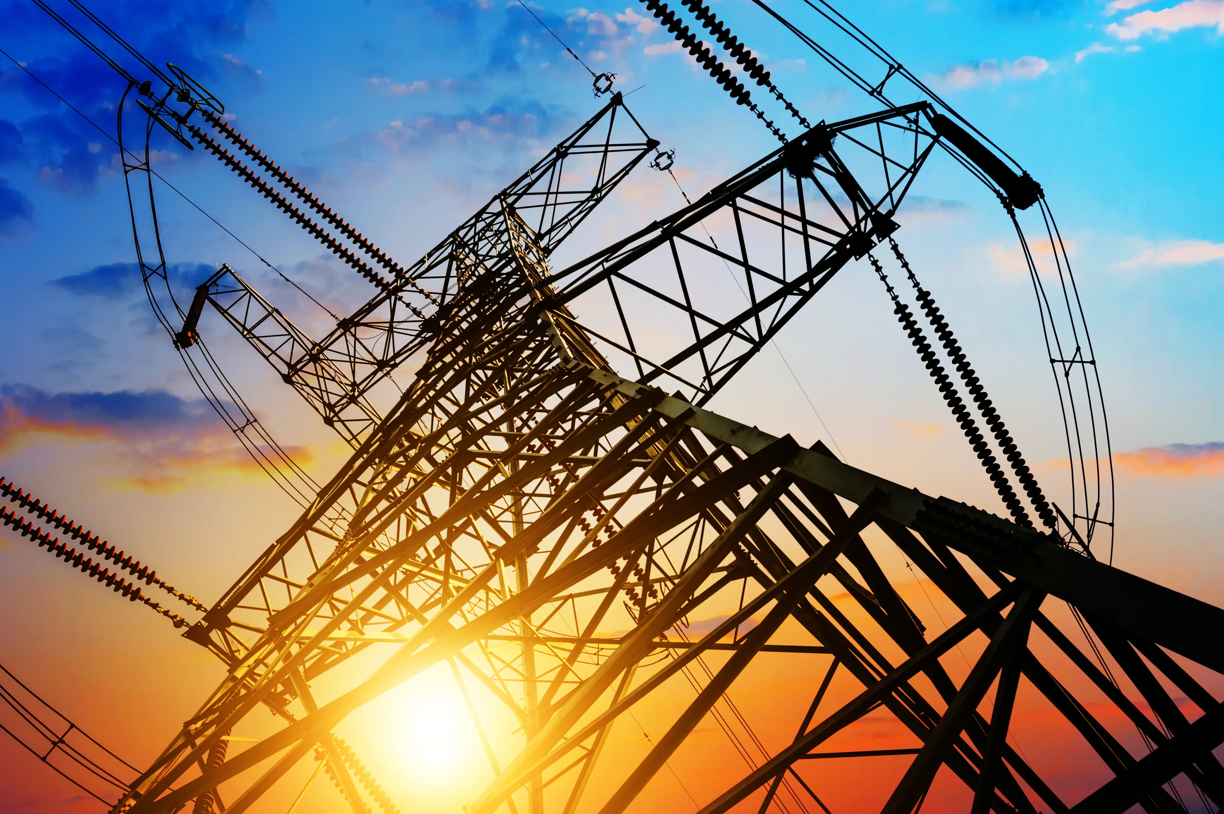 A silhouette of an electricity pylon against a vibrant sunset sky, with hues of orange, pink, and blue.