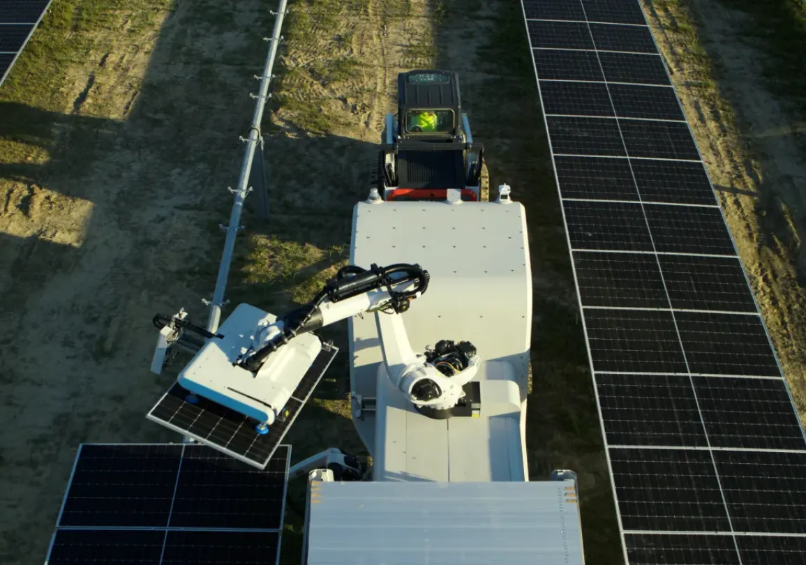 Aerial view of a solar panel installation with a robotic arm and a worker in a safety vest and hard hat inspecting the area.